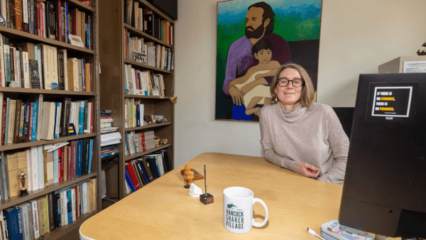 Dr. Pavão-Zuckerman sitting at her office desk smiling. Her office shows two bookshelves full of books and a painting of a son and father. 