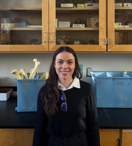 Fernanda standing in front of ancient human species cranium replicas at 0124B Laboratory at Woods Hall.