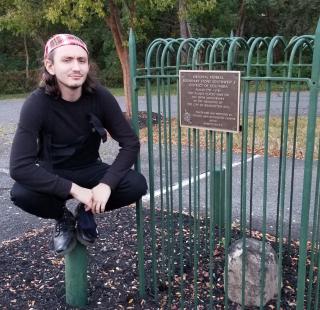 Man balancing on pole next to encaged decrepit boundary stone