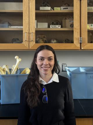 Fernanda is standing in front of osteological material, at the 0124B laboratory at Woods Hall.