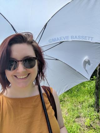 Maeve standing with sunglasses under a white umbrella